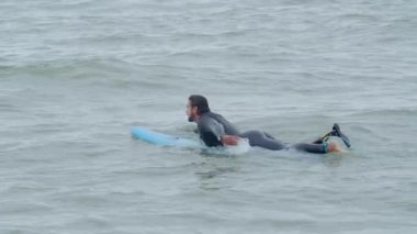 Denizde sörf tahtasında yatan yapay bacaklı bir sporcu.
