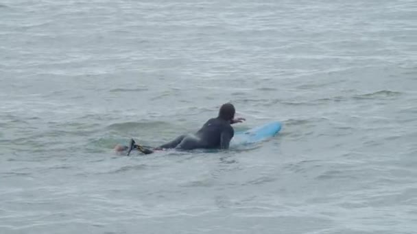 Atleta enfocado con pierna artificial acostado en la tabla de surf en el océano — Vídeos de Stock