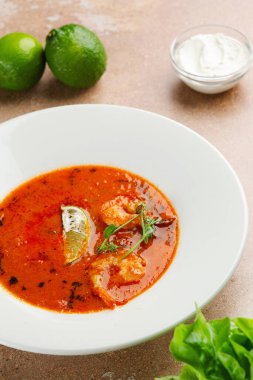 Beton arka planda beyaz plakalı Tom yum. Baharatlı Tayland yemeği ve masada malzemeler. Baharatlı Tayland yemeği.