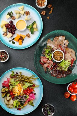 Koyu beton arka plan manzaralı üç tabaklı şarküteri masası. Bal ve üzümlü peynir tabağı, salamura sebze tabağı, jambon tabağı..