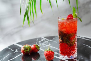 Mermer masada nane yaprağı olan çilekli mojito. Arka planda çilekli ve tropik dallı taze içecekler.
