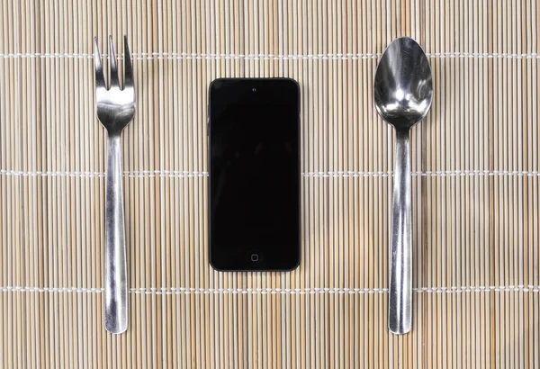 Smartphone with fork and spoon on bamboo mat background — Stock Photo, Image