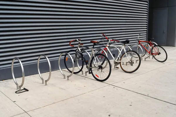 Trois vélos sont verrouillés sur les supports de trottoir Photo De Stock