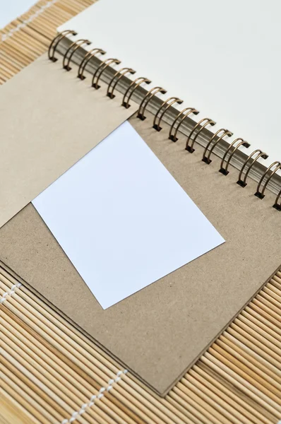 Bloc de notas en blanco con un pedazo de papel sobre fondo de estera de bambú —  Fotos de Stock