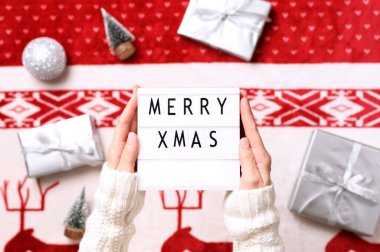 Işıkkutusuna yakın plan, ellerinde mutlu noeller ve arka planda Noel hediyeleri, minyatür ağaçlar. Üst görünüm