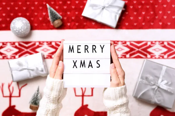 Primer plano de la caja de luz con texto feliz Navidad en las manos y el fondo con regalos de Navidad, árboles en miniatura. Vista superior —  Fotos de Stock