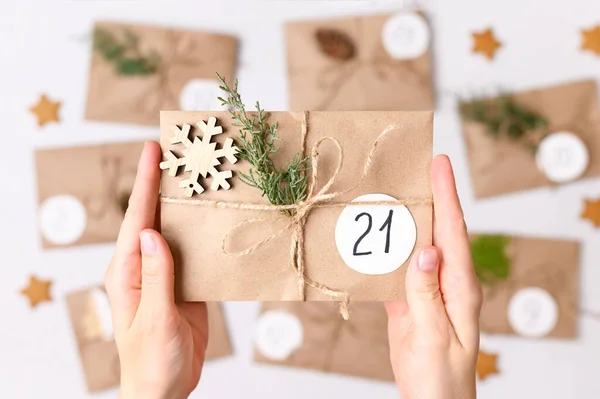 Świąteczny kalendarz. Kobiece dłonie robiące prezenty z kopert kraft, gałązek jodły, szyszek sosny. Widok z góry — Zdjęcie stockowe