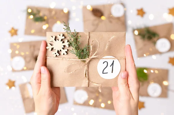 Calendario de Adviento de Navidad. Mujeres manos haciendo regalos con sobres kraft, ramas de abeto, conos de pino. Vista superior —  Fotos de Stock