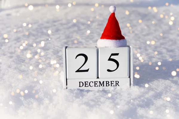 Cocepto de Navidad. 25 de diciembre números de calendario y sombrero de Santa sobre fondo de nieve con luces. —  Fotos de Stock