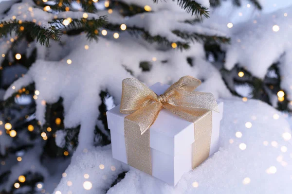 Prezent świąteczny na tle drzewa i śniegu ze światłami — Zdjęcie stockowe