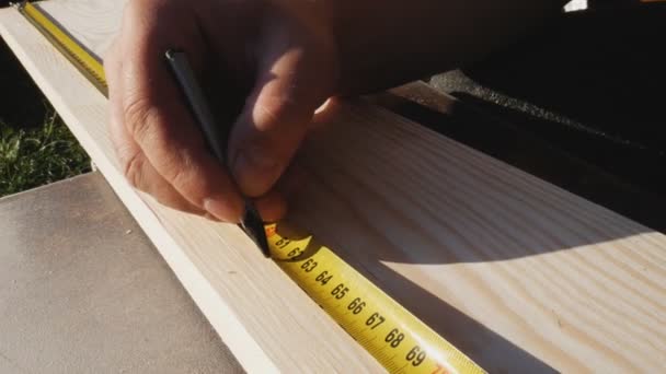 À l'aide d'une règle, le travailleur marque les dimensions avec un crayon. Ruban jaune, rouleau de ruban à mesurer. Préparation des dimensions de la planche pour un traitement ultérieur — Video