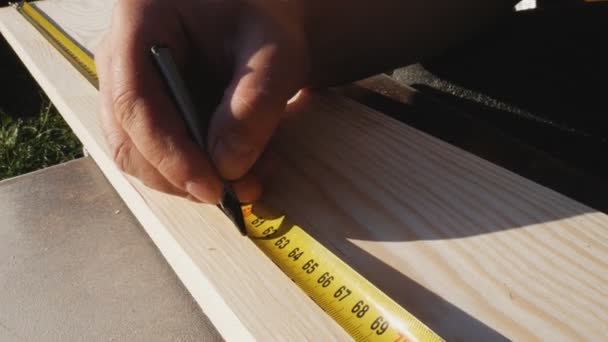 Using a ruler, the worker marks the dimensions with a pencil. Yellow tape measure, roll of measuring tape. Preparing the dimensions of the board for subsequent processing — Stockvideo