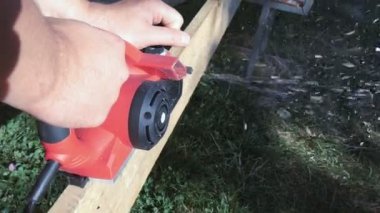 Elektrikli uçağın ahşap kalaslarını planlamak. Bir marangoz elektrikli bir alet kullanarak tahta kalaslarla çalışır.