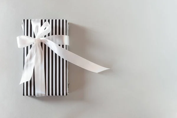 黒と白のストライプのパッケージをギフト 白いサテンリボン付きの厳格なモノクロギフトのトップビュー 男のための誕生日カードの概念的なミニマルなデザイン 父の日 クリスマス スペースのコピー — ストック写真