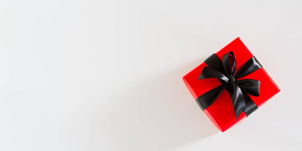 Gift black and red packaging. Top view of a bright gift with a black satin ribbon on a white background. Conceptual minimalistic banner design for Birthday, Christmas, Valentine's Day. Copy space