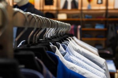 Gömlekler askılara yakın çekim yapıyor. Erkek giyim mağazası, çeşitli sonbahar-kış ürünleri var. Butikteki malların çeşitliliği. Satış, terfi, Kara Cuma konsepti.