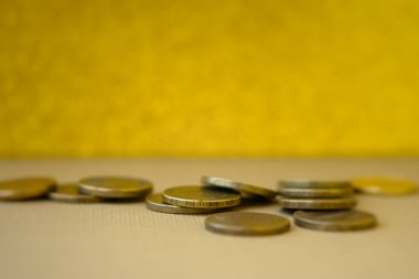 Bozuk paralar grubuna yakın çekim. Yumuşak seçici odak noktasında parlak paralar. Arka plan hardal sarısı, kopyalama alanı. Sıcak sonbahar gölgeleri, zenginlik konsepti, refah, başarı. Bir yığın bozuk para dağıtıldı.