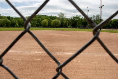 looking through a Galvanized Chain Link fence baseball clay dirt white caulk line and footprints with grass and trees