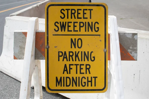 street sweeping no parking after midnight yellow black street sign with blocking plastic street dividers or Barricades