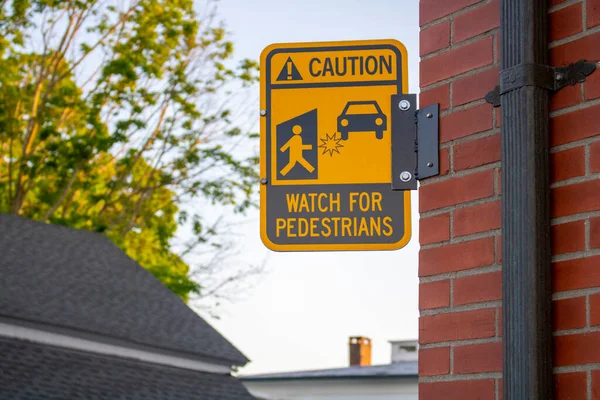 pedestrians yellow black street sign Caution watch for pedestrians in suburban area on a side of a brick building