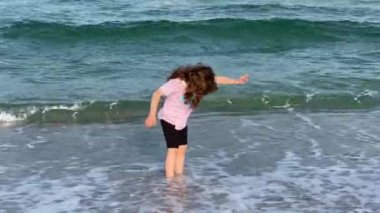 Bir kız plaj ayakkabılarında dalgalarla eğleniyor.