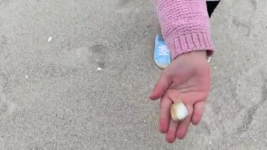 Tatilde olan genç bir kız kabuğu sıkıca kapalı canlı bir midye bulur ve onu kameraya gösterir ve şakacıdır ve onu yer gibi yapar.
