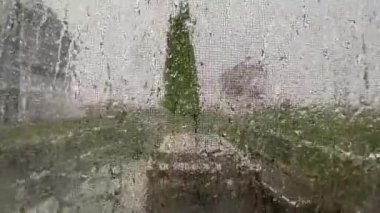 Metal bir ekran penceresinden büyük bir sağanak yağış esiyor ve yağmur yağıyor.