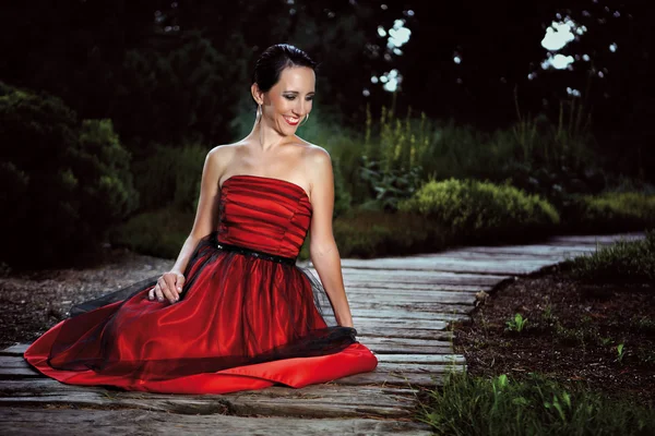 Lady in red dress posing in garden — Stock Photo, Image