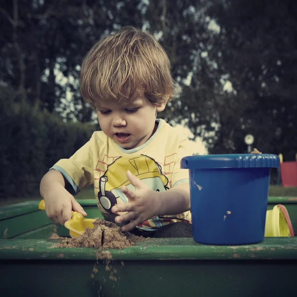 Ung pojke spelar hemma nära house i trädgård med olika leksaker — Stockfoto