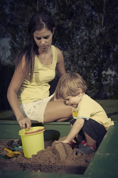 Jonge jongen thuis spelen in de buurt van huis in de tuin met zijn moeder met verschillende speelgoed — Stockfoto