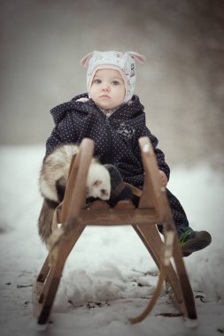 Bir yaşında bir bebek, dağ gelinciği arkadaşıyla tahta bir kızağın üstünde.
