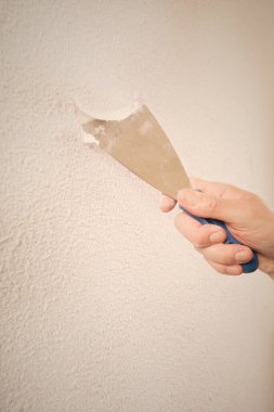 Older man removing old wallpapers off the walls in empty apartment