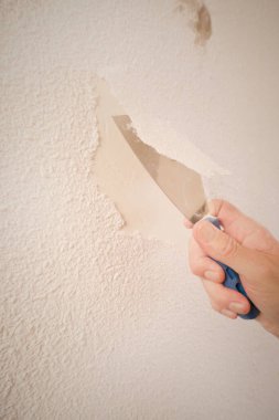 Older man removing old wallpapers off the walls in empty apartment
