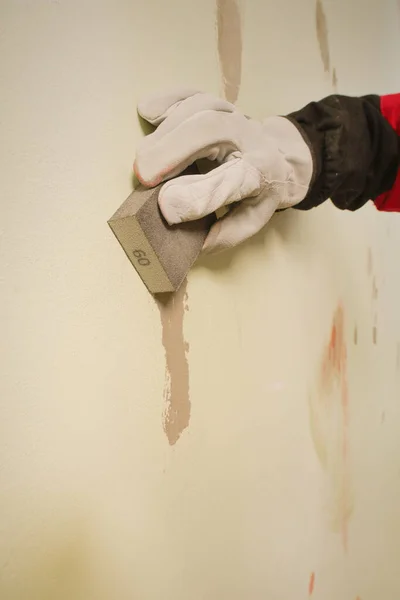Older man working in empty apartment sanding repair walls before painting