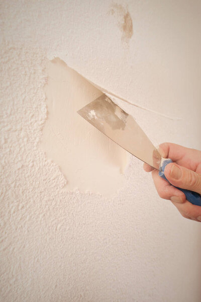 Older man removing old wallpapers off the walls in empty apartment