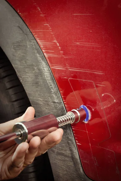 Car owner working on a dent repair with reverse hammer and glue