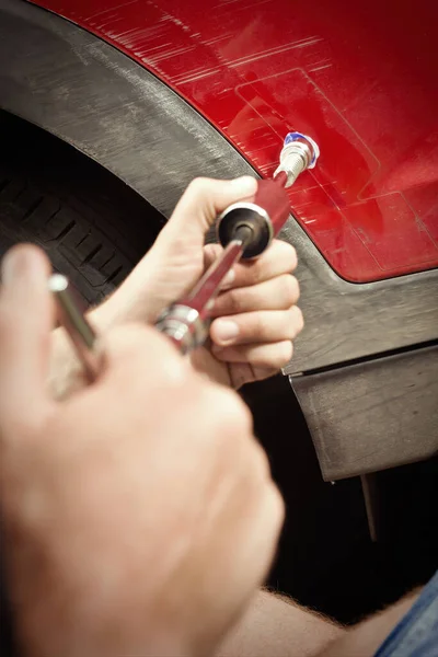 Car owner working on a dent repair with reverse hammer and glue