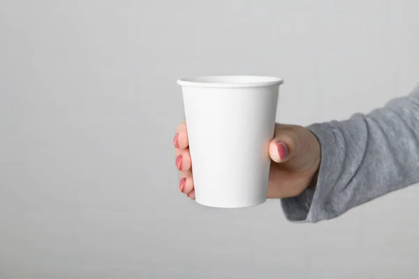Рука женщины держит пустую пустую бумажную чашку на нейтральном сером фоне. — стоковое фото
