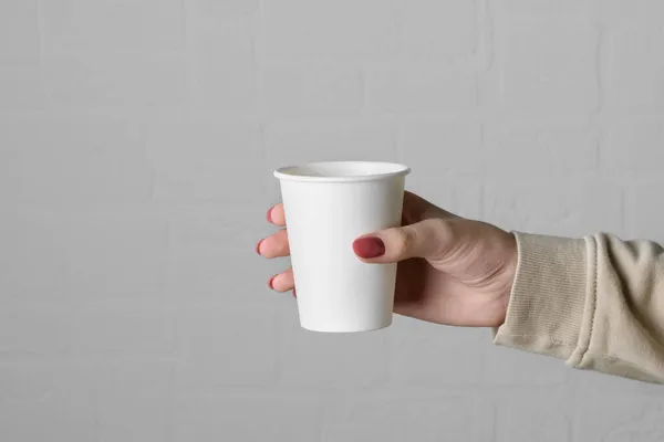 Θηλυκό χέρι κρατώντας κενό Πάρτε μακριά χάρτινο κύπελλο σε ουδέτερο γκρι φόντο τοίχο — Φωτογραφία Αρχείου