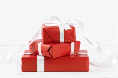 Beyaz ahşap arka planda beyaz kurdeleli üç kırmızı hediye kutusunu kapatın, kopyalayın. Noel ya da Sevgililer Günü hediyesi