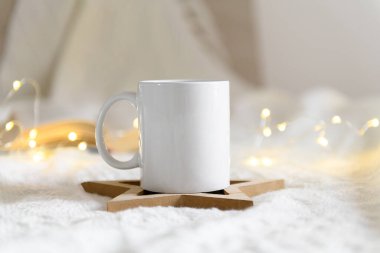 Boş fotokopi alanı olan beyaz kupa modeli. Bej kaplı arka planda kahve fincanı açık kitap ve Noel süsleri, sarılma evinde sıcak bir kış günü.