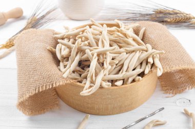 Whole grain wheat raw apulian pasta called Pizzarieddi or maccaruni in a sieve on white wooden table. Fresh maccheroni typical dish of Puglia, Salento Italy. Italian homemade pasta background