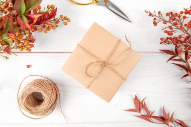 Autumn creative holiday present. Handmade paper gift box with red e orange foliage leaves, on white wooden background. Thanksgiving day, fall background. top view, flat lay