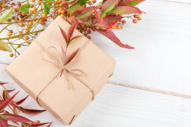 Autumn creative holiday present. Handmade paper gift box with red e orange foliage leaves, on white wooden background. Thanksgiving day, fall background. Copy space