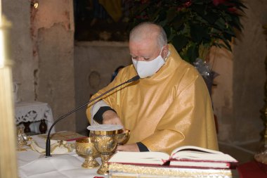 SAN PIETRO, İTALYA - 26, 2021. Başrahip bir yüz maskesi takmış ayinin kutlaması için hazırlanıyor, ayin sırasında mihrapta kutsal bir ev sahibi tutuyor.