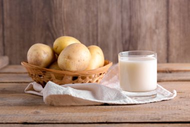 Bardakta vejetaryen patates sütü ve kahverengi ahşap arka planda patates yumrusu. Kapatın. Bitki bazlı alternatif süt değiştirici ve laktozsuz, sağlıklı vejetaryen ve vejetaryen içecek konsepti