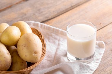 Bardakta vejetaryen patates sütü ve kahverengi ahşap arka planda patates yumrusu. Kapatın. Bitki bazlı alternatif süt değiştirici ve laktozsuz, sağlıklı vejetaryen ve vejetaryen içecek konsepti