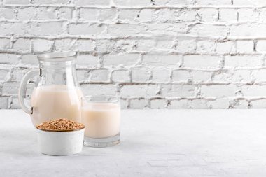 Vejetaryen günlük olmayan karabuğday sütü ve karabuğdaylı bardak beyaz taş bir masada bir kase inliyor. Vegan karabuğday içeceği, bitki bazlı alternatif süttür. Sebzeler sürahide sağlıklı süt ürünü