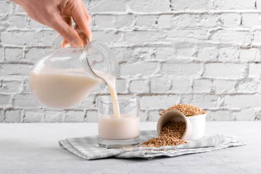 Vejetaryen olmayan karabuğday sütü bardağa dökülüyor, yanında karabuğday, beyaz bir taş masada bir kase inliyor. Vegan karabuğday içeceği, bitki bazlı alternatif süttür. Sebzeler sağlıklı süt ürünü