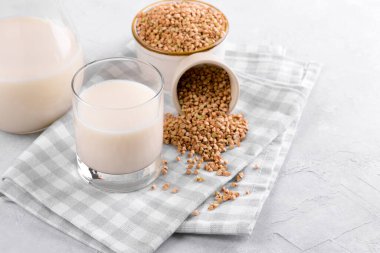 Vegan günlük olmayan karabuğday sütü bardakta, karabuğday filizleri kasede ve beyaz taş masada. Vegan karabuğday içeceği, bitki bazlı alternatif süttür. Sebzeler sağlıklı süt ürünü, seçici odaklanma